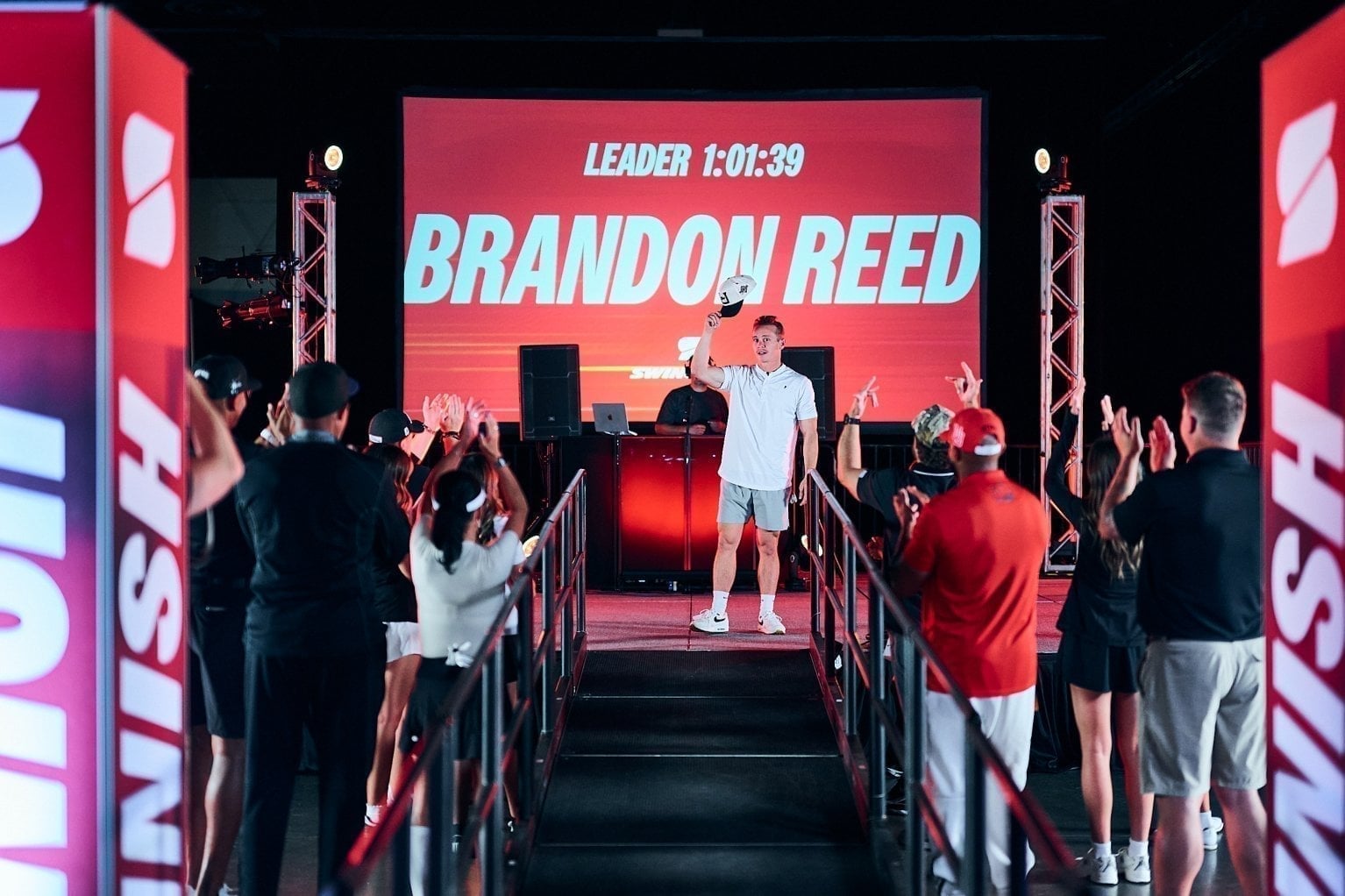 A golfer crosses the finish line under the live leaderboard as the crowd cheers