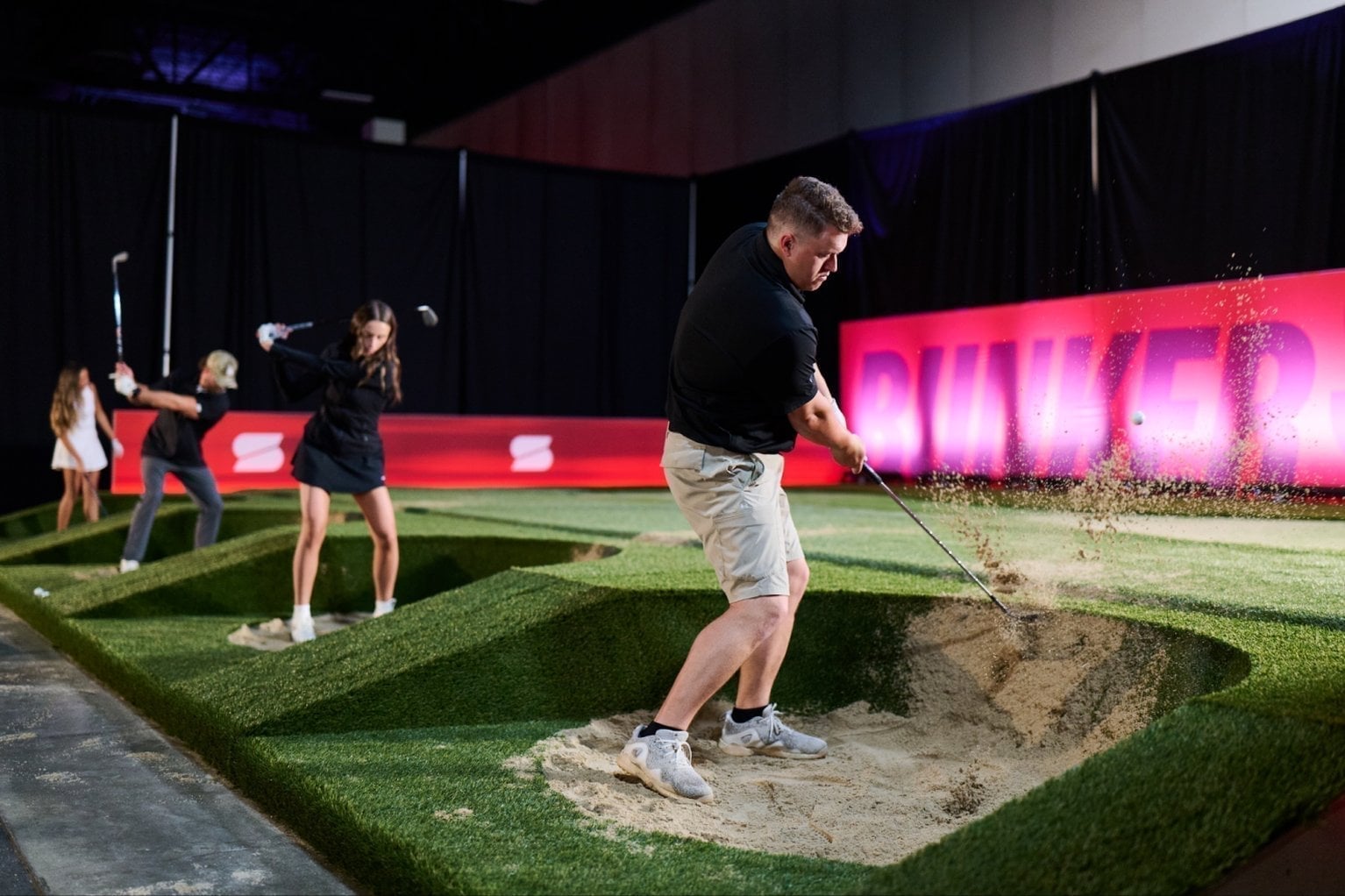 Golfers play out of a bunker on the arena course