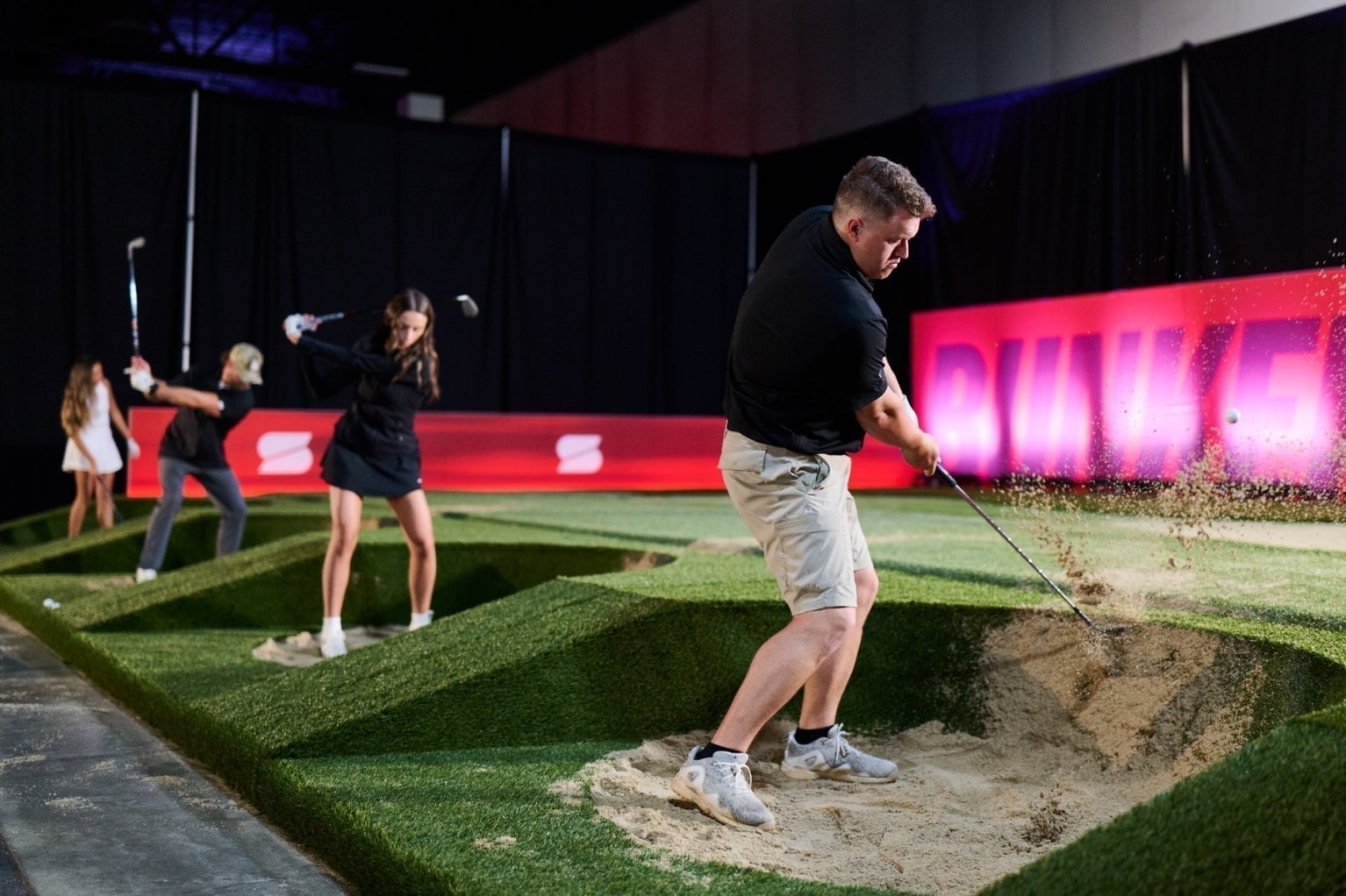 Golfers play out of a bunker on the arena course