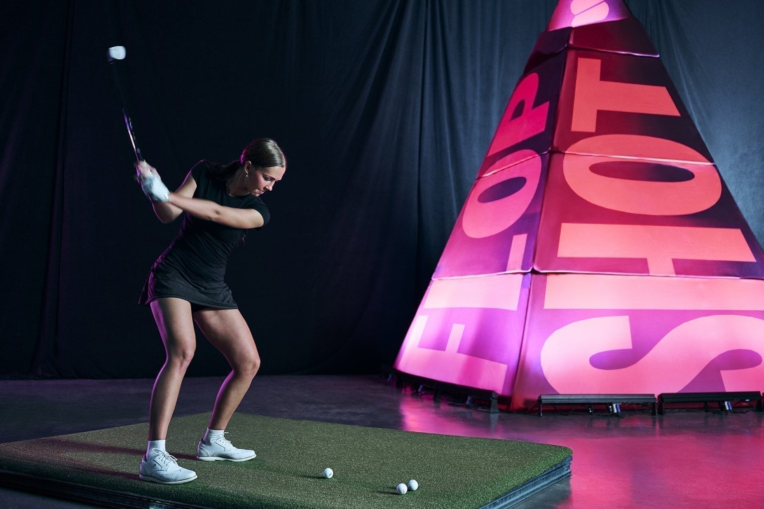 A golfer swings on an arena tee box beside a glowing Swingrush target