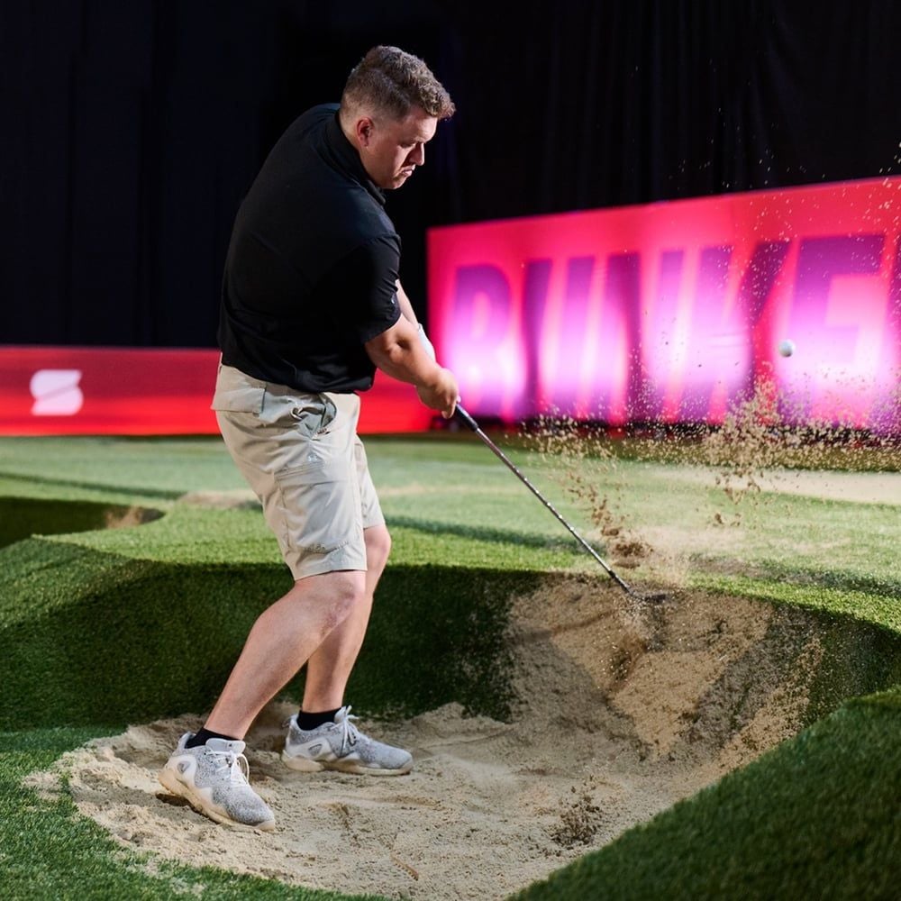 A golfer hitting out of a bunker in front of a pink bunker sign